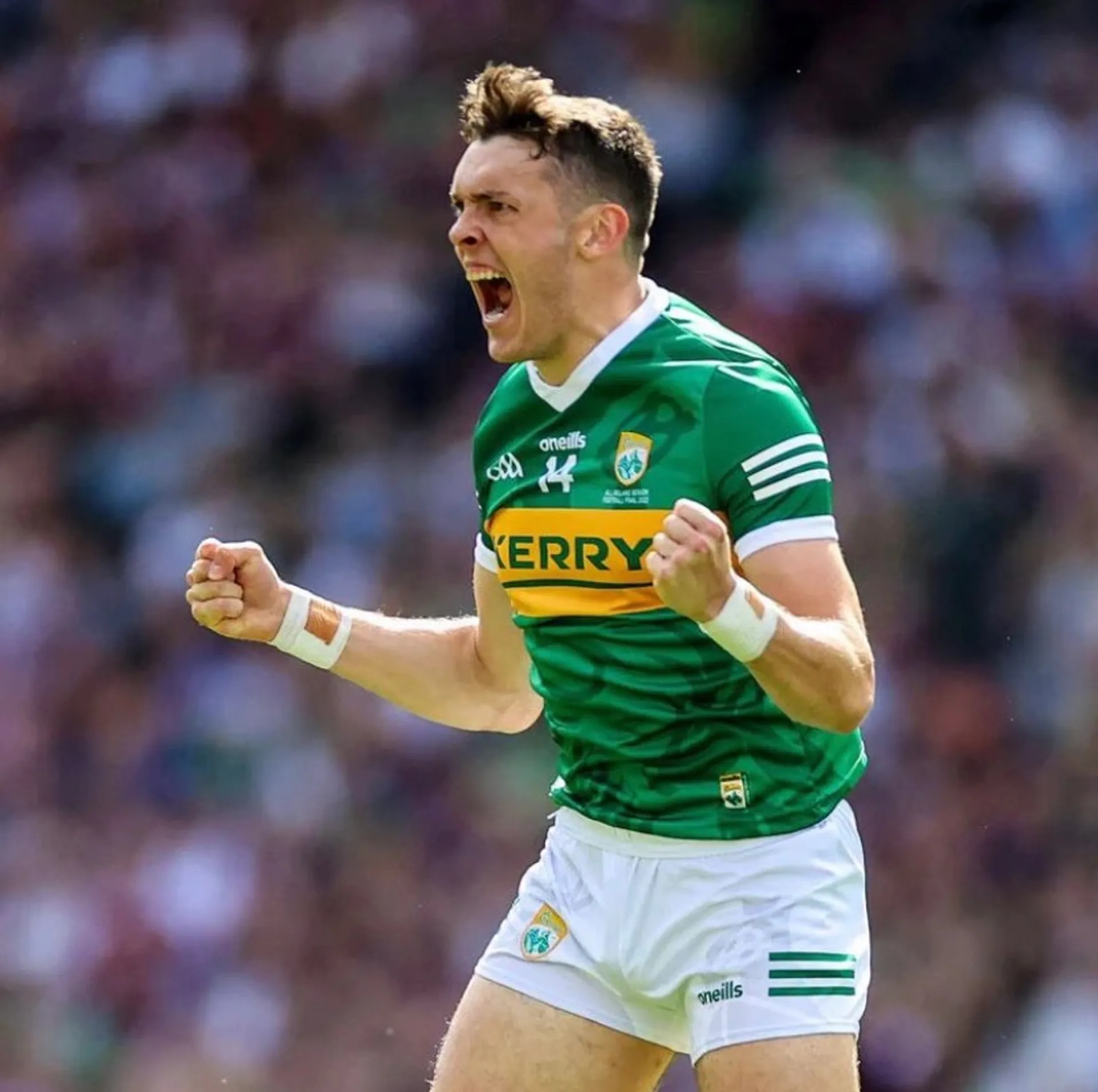 Kerry footballer celebrating after a score, fists clenched, packed crowd behind